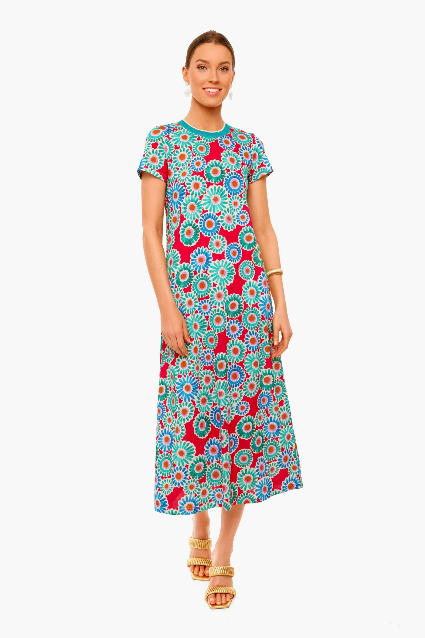 A woman wears a colorful La DoubleJ short-sleeve, ankle-length vintage floral dress with red, blue, and green patterns, paired with gold wedge sandals and a gold bracelet for an Italian-inspired look.