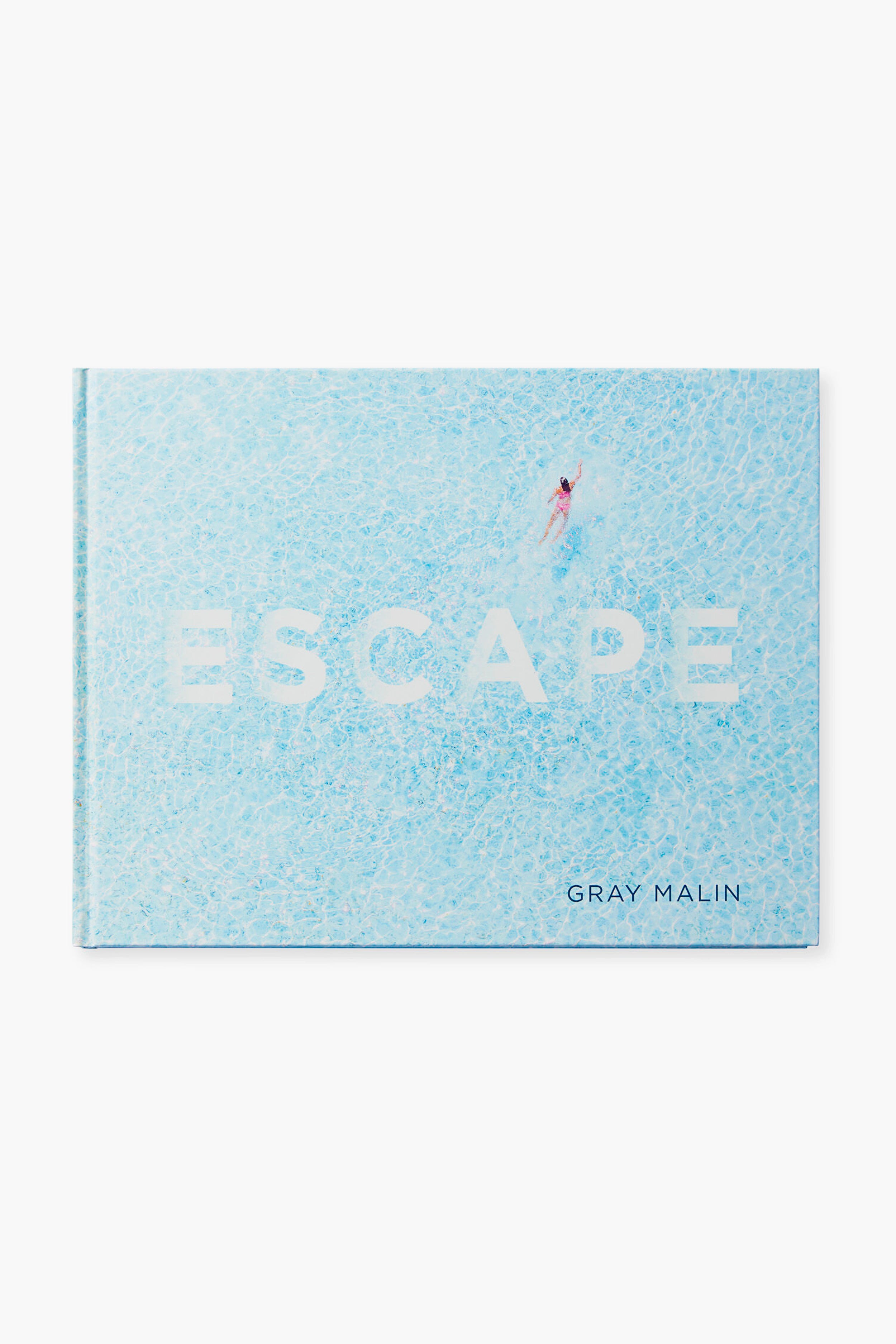 Rizzoli's book ESCAPE by Gray Malin showcases stunning travel photography, with a cover featuring a swimmer in a clear blue pool that evokes the beauty of exotic vacation spots.