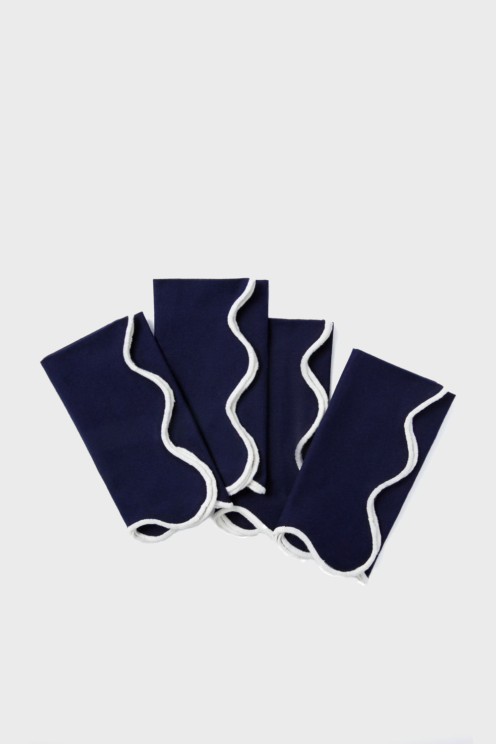 Four neatly folded Tuckernuck Home dark blue scalloped napkins with white wavy trim are arranged in a fanned-out pattern.