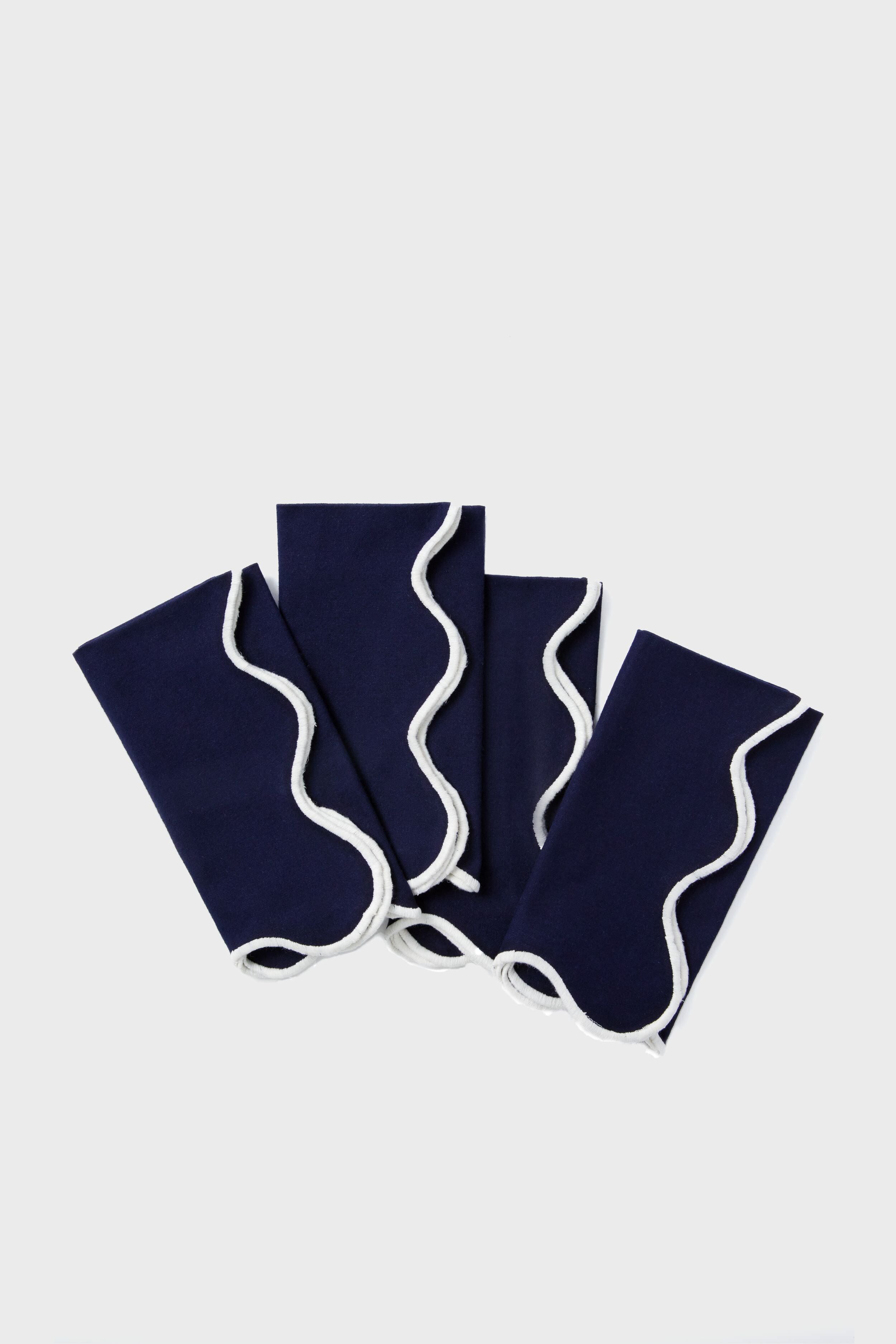 Four neatly folded Tuckernuck Home dark blue scalloped napkins with white wavy trim are arranged in a fanned-out pattern.