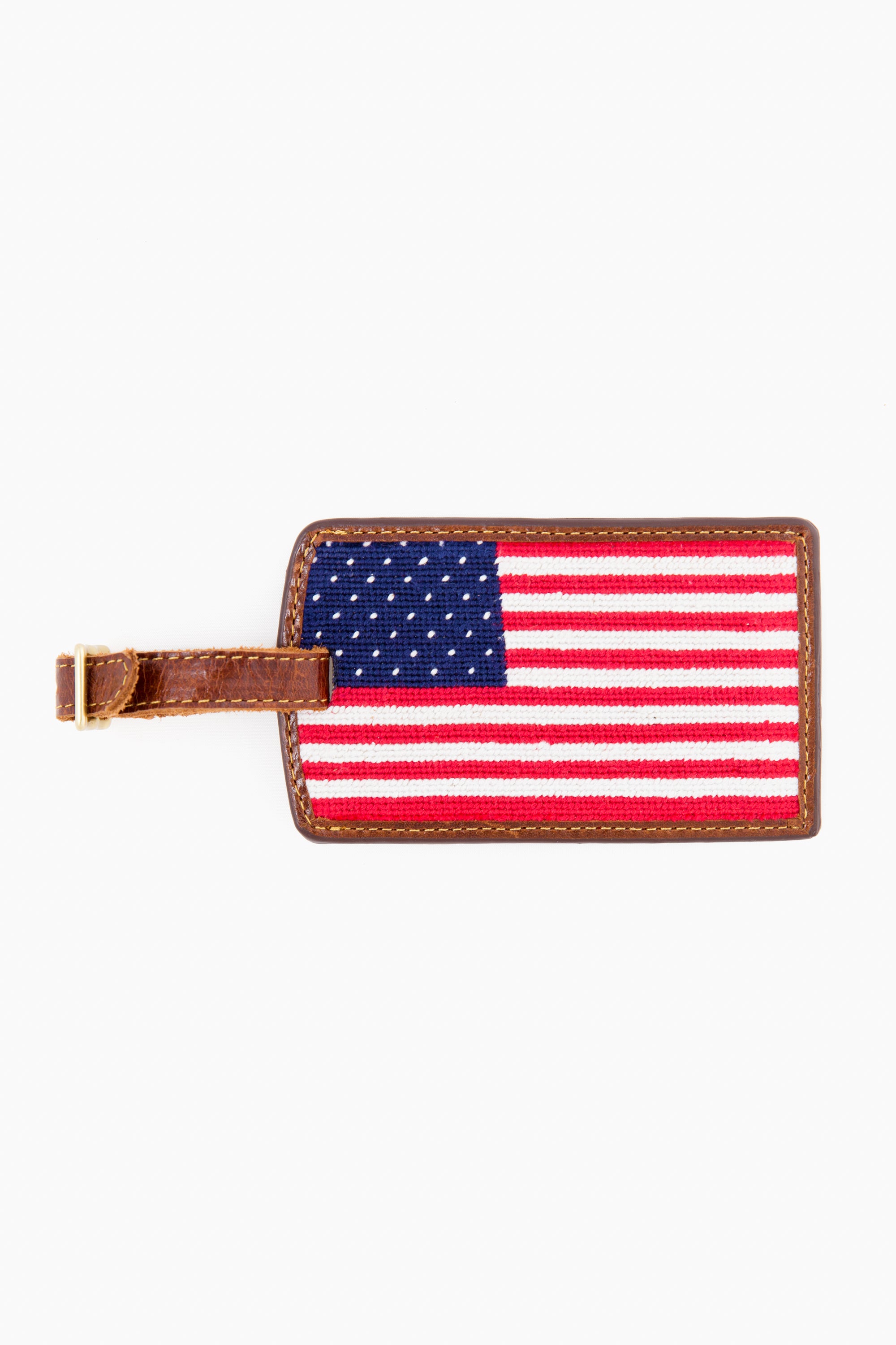 The Smathers and Branson rectangular American Flag Needlepoint Luggage Tag features hand-stitched needlepoint and a brown leather strap, making it a stylish travel accessory.