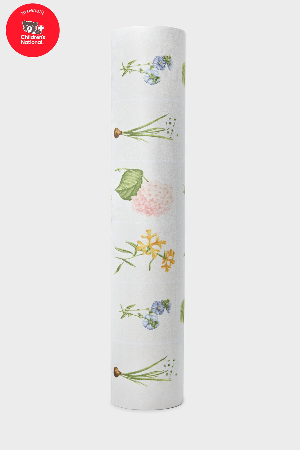 A roll of white Tuckernuck x Jollie gift wrap with colorful floral illustrations is shown. A Childrens National Hospital benefit badge appears in the upper left, inspired by the Fresh Buds Yoga Mat design.