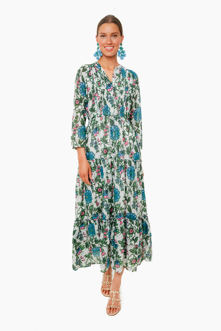 A woman in a Banjanan long organic cotton floral dress with blue and green patterns, handmade embroidery, blue statement earrings, and studded sandals.