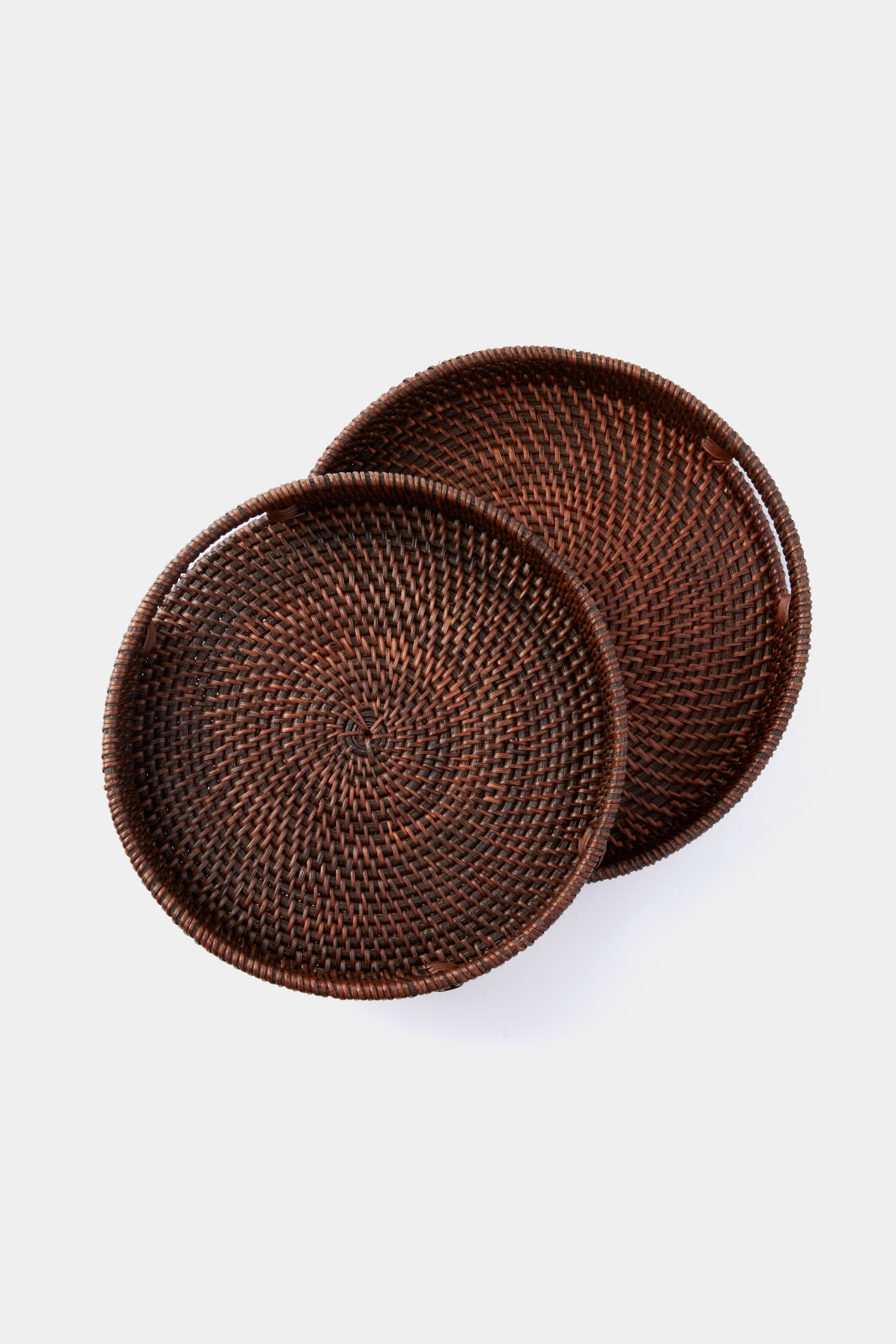 Two round, dark brown rattan woven texture trays by Tuckernuck Home overlap each other, making them perfect as unique hostess gifts.