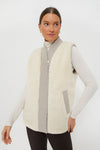 A person wears a sleeveless cream Varley quilted reversible gilet over a long-sleeve white turtleneck and dark pants.