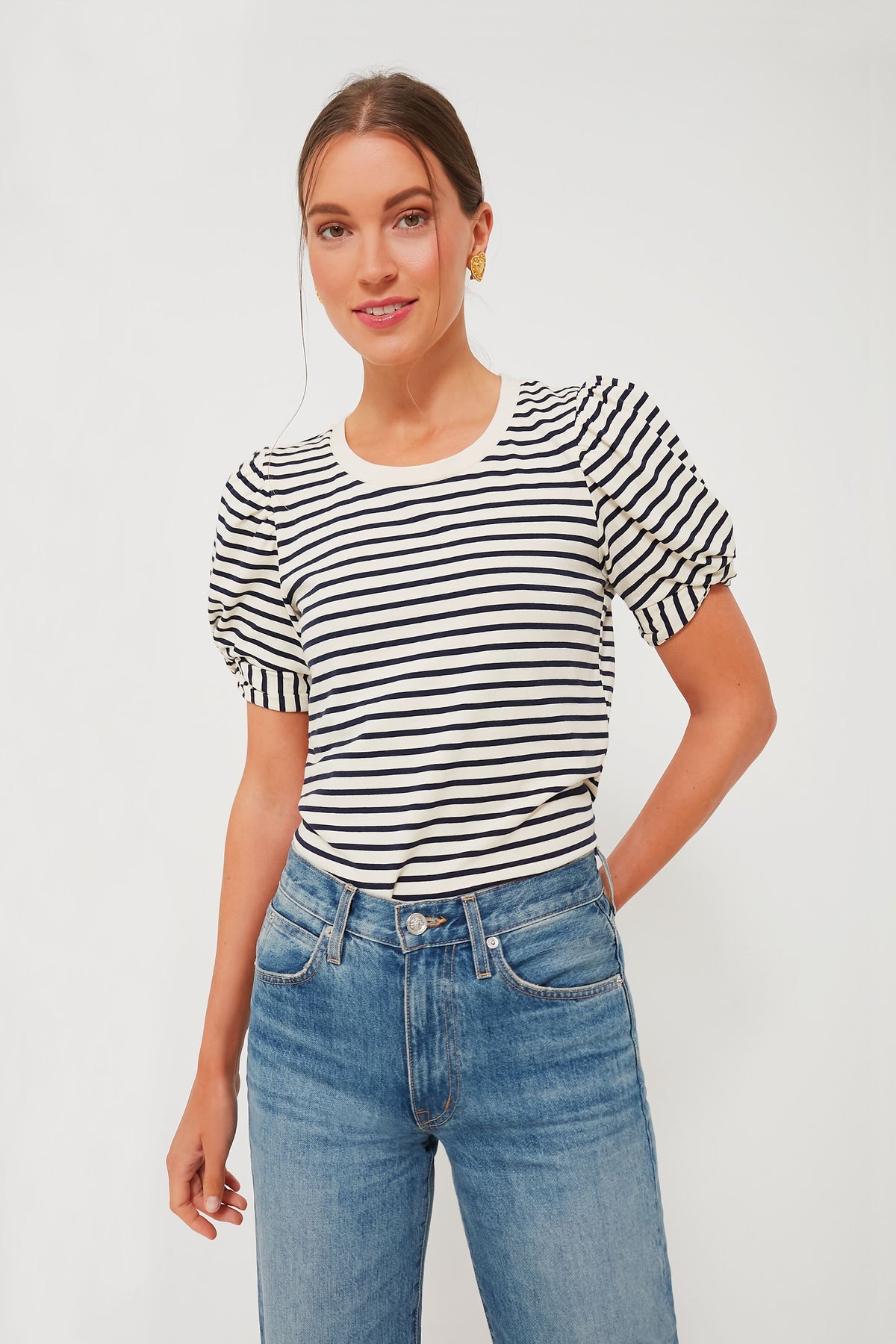 A woman stands confidently in a Pomander Place loose-fit crewneck top with black and navy stripes, puff short sleeves, and blue jeans.