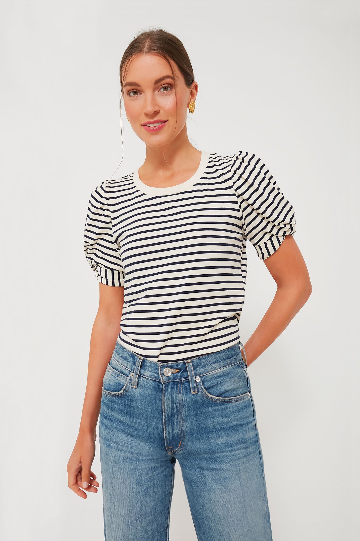 A woman stands confidently in a Pomander Place loose-fit crewneck top with black and navy stripes, puff short sleeves, and blue jeans.