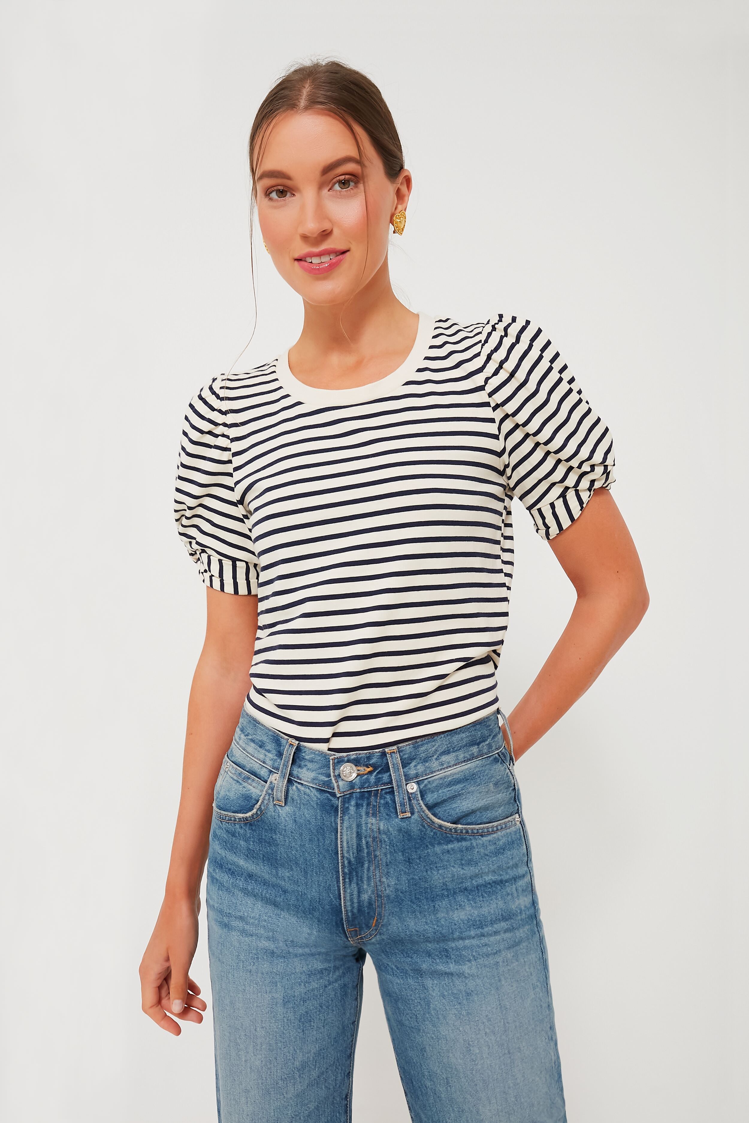 A woman stands confidently in a Pomander Place loose-fit crewneck top with black and navy stripes, puff short sleeves, and blue jeans.