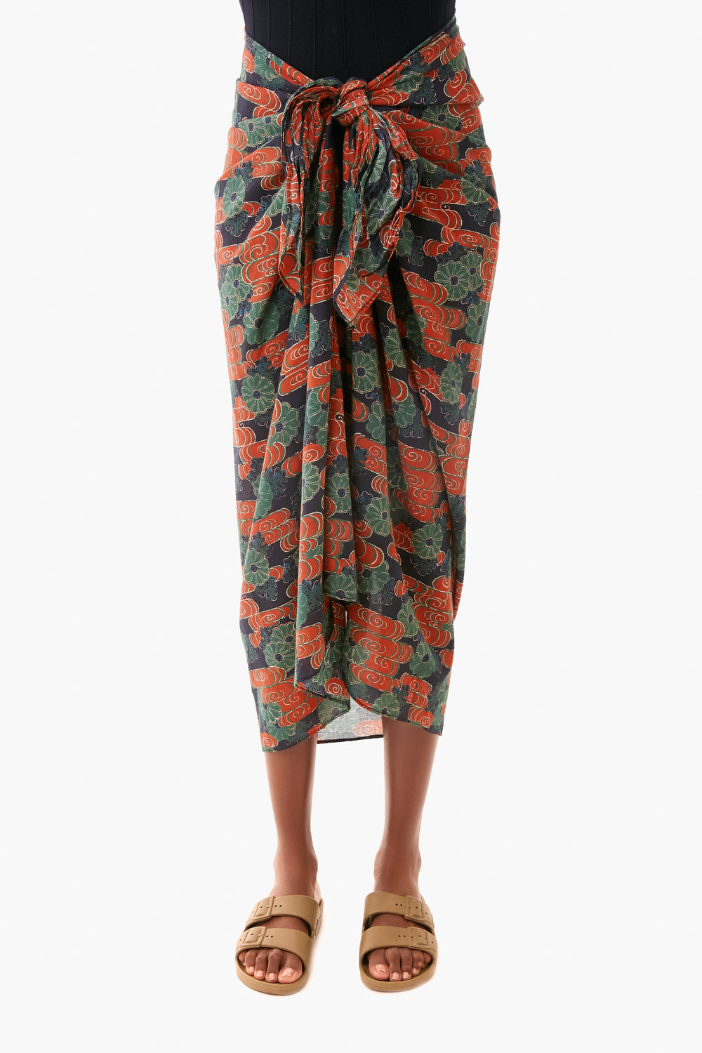 Wearing a Ulla Johnson black top, floral sarong with red and green accents tied at the waist, and tan sandals, this look makes the perfect vacation coverup and radiates confidence.