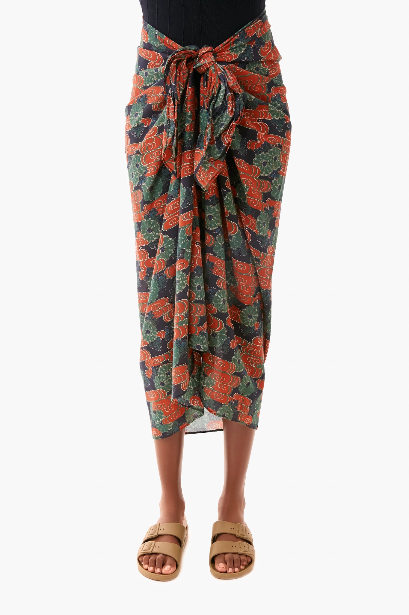 Wearing a Ulla Johnson black top, floral sarong with red and green accents tied at the waist, and tan sandals, this look makes the perfect vacation coverup and radiates confidence.