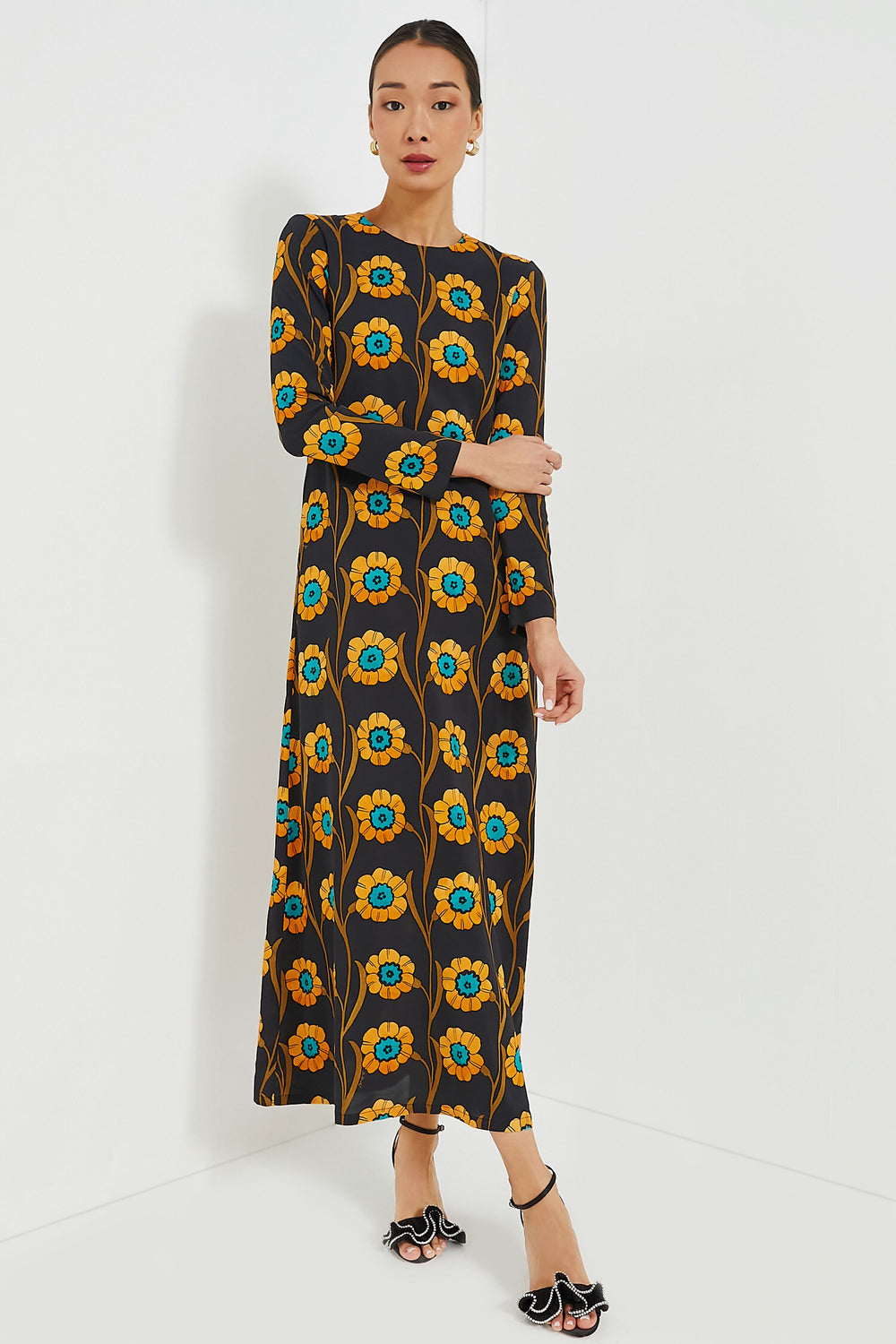 A woman wears a La DoubleJ maxi swing dress with long sleeves and a bold blue and yellow floral print, paired with black heeled sandals. This eye-catching piece is crafted in Italy by La DoubleJ.