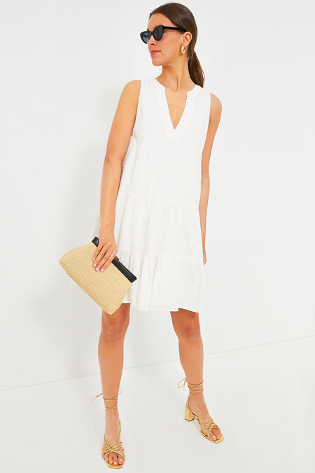 A woman stands with effortless poise in a Pomander Place sleeveless summer dress in white, paired with gold strappy sandals, sunglasses, and a woven clutch.