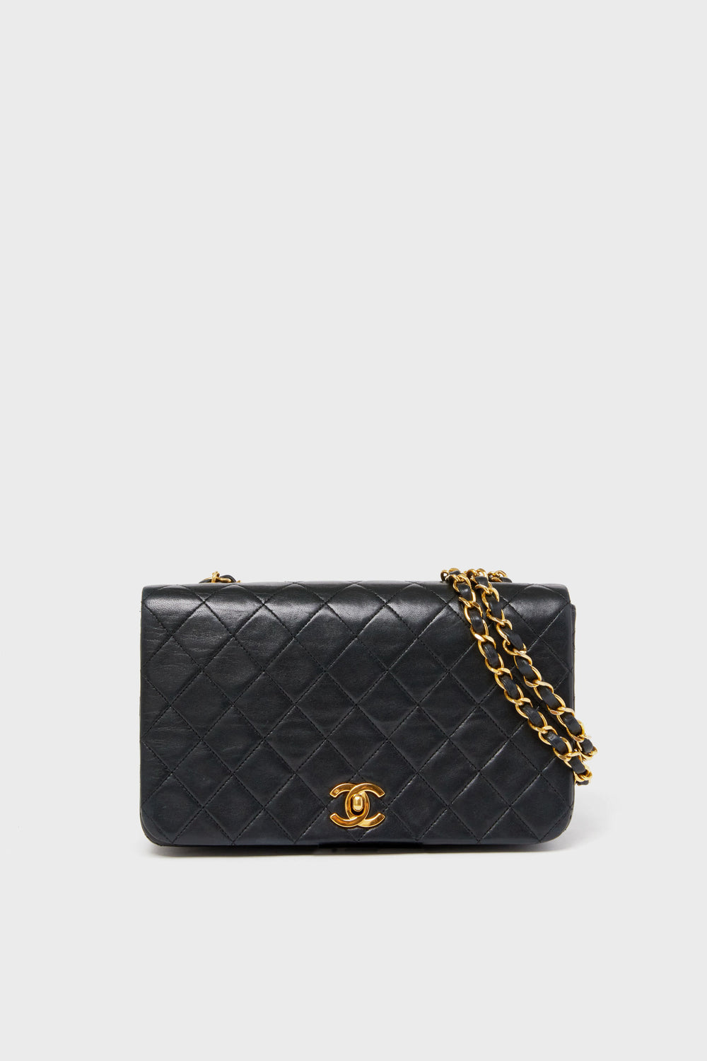 A black Tuckernuck Archive Collection Classic Flap Bag in quilted lambskin with a gold chain strap and gold clasp featuring the signature logo.