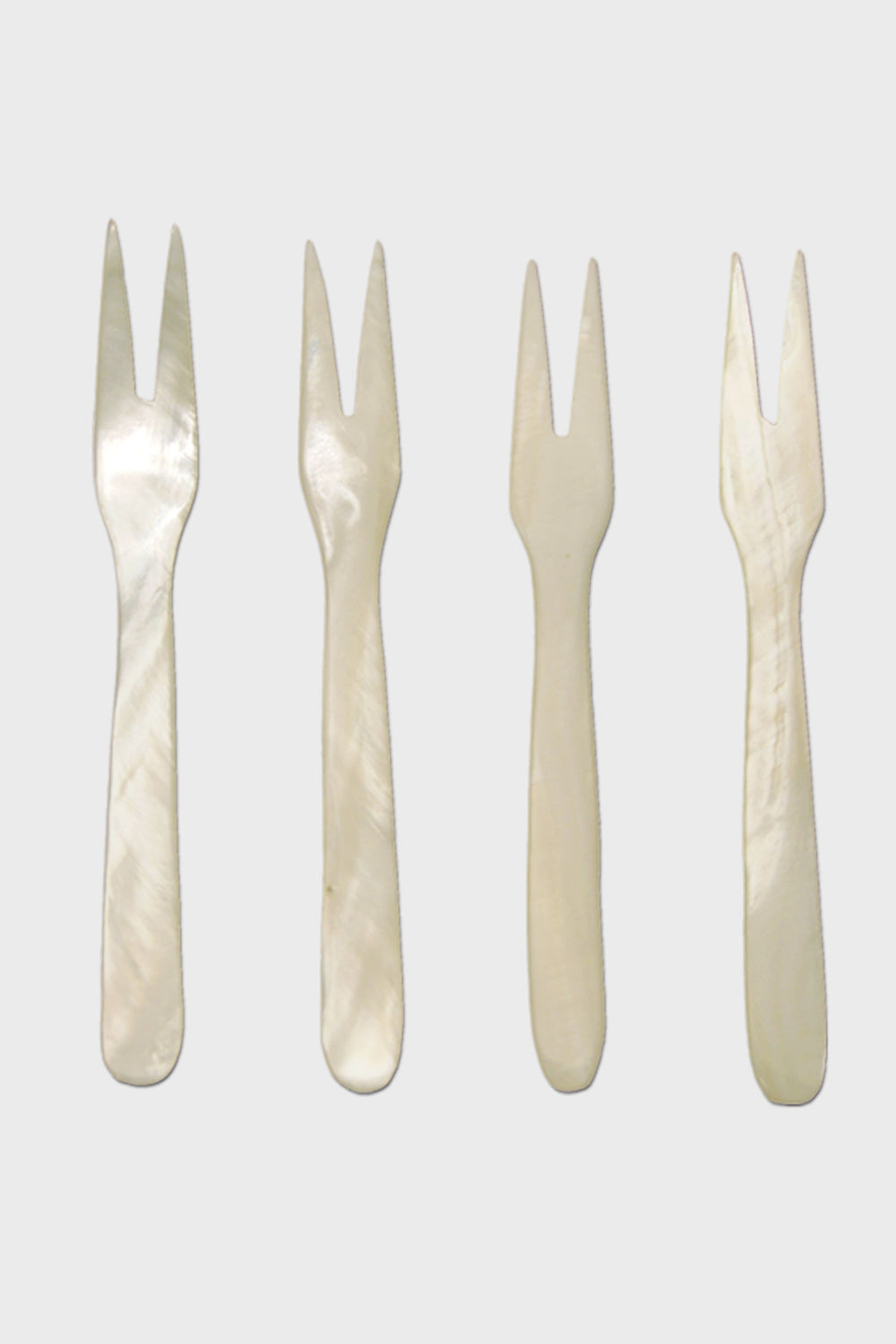 Four small, two-pronged, white mother-of-pearl seashell forks by Be Home are arranged in a row—perfect for coastal dining and for adding ethically sourced elegance to your home.