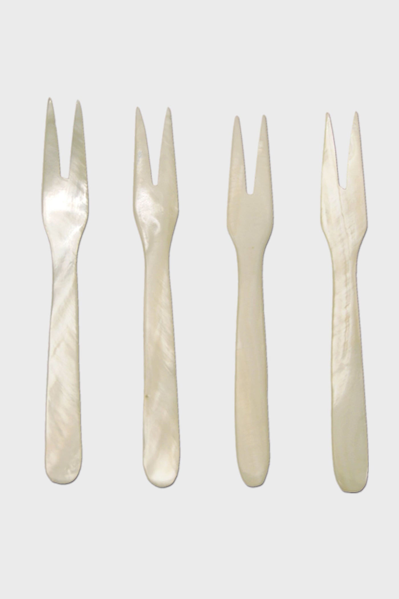 Four small, two-pronged, white mother-of-pearl seashell forks by Be Home are arranged in a row—perfect for coastal dining and for adding ethically sourced elegance to your home.