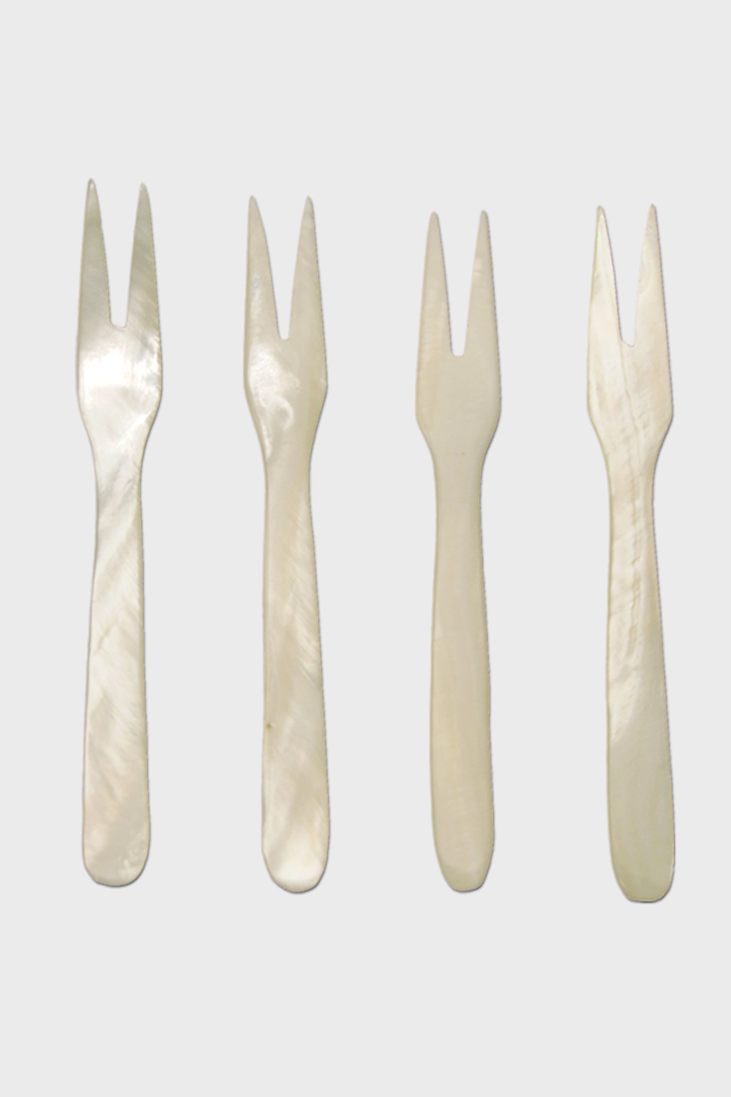Four small, two-pronged, white mother-of-pearl seashell forks by Be Home are arranged in a row—perfect for coastal dining and for adding ethically sourced elegance to your home.