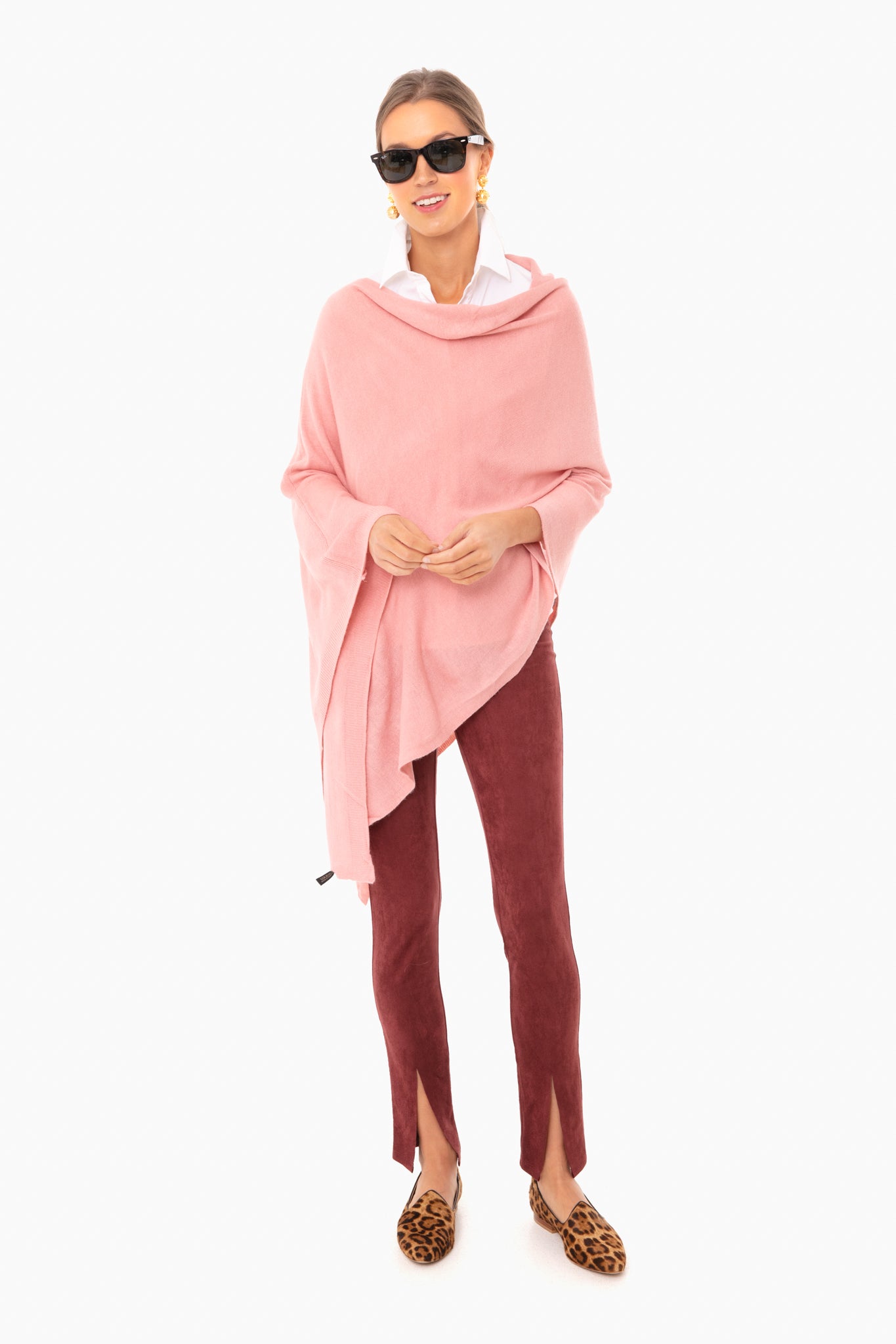 A woman in a Pomander Place pink layering poncho, white shirt, burgundy pants with front slits, leopard print loafers, sunglasses, and gold earrings—an ideal look for al fresco dining.