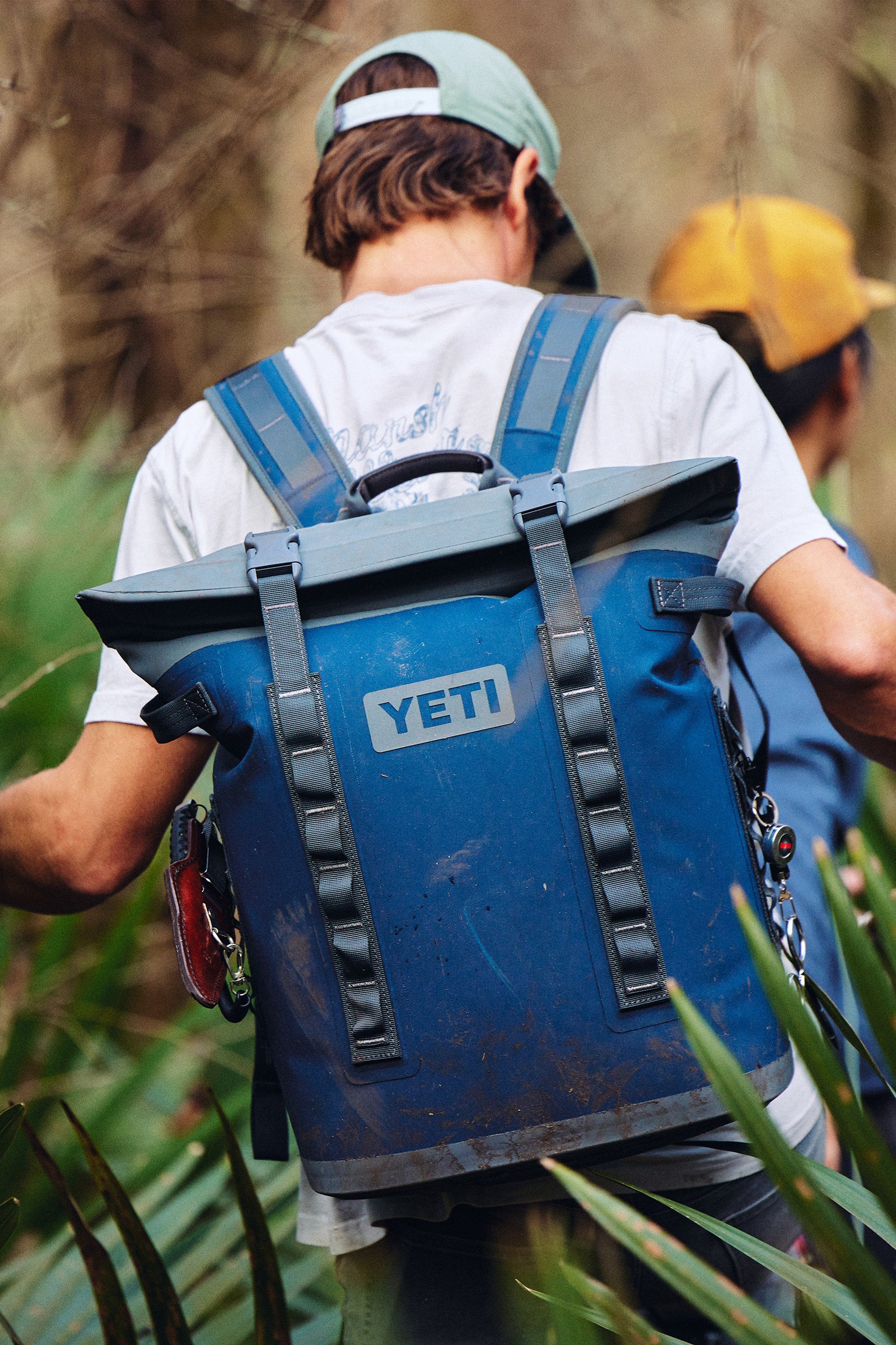 Person trekking through foliage with a classic, effortless YETI Navy Hopper M20 Backpack, perfect for fun, high-end outdoor adventures, showcasing its hands-free, innovative design.