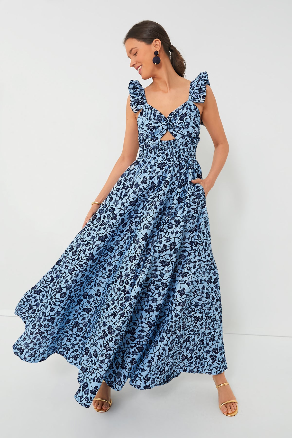 A woman wearing the elisamama Exclusive Blue Ibukun Dress, a handmade Nigerian piece with ruffled sleeves and abstract floral print, looks down with a soft smile.