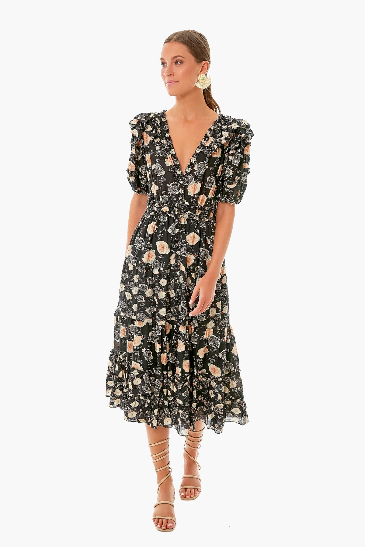 Woman in a black floral Ulla Johnson dress featuring short puff sleeves and a deep V-neckline, paired with strappy sandals.