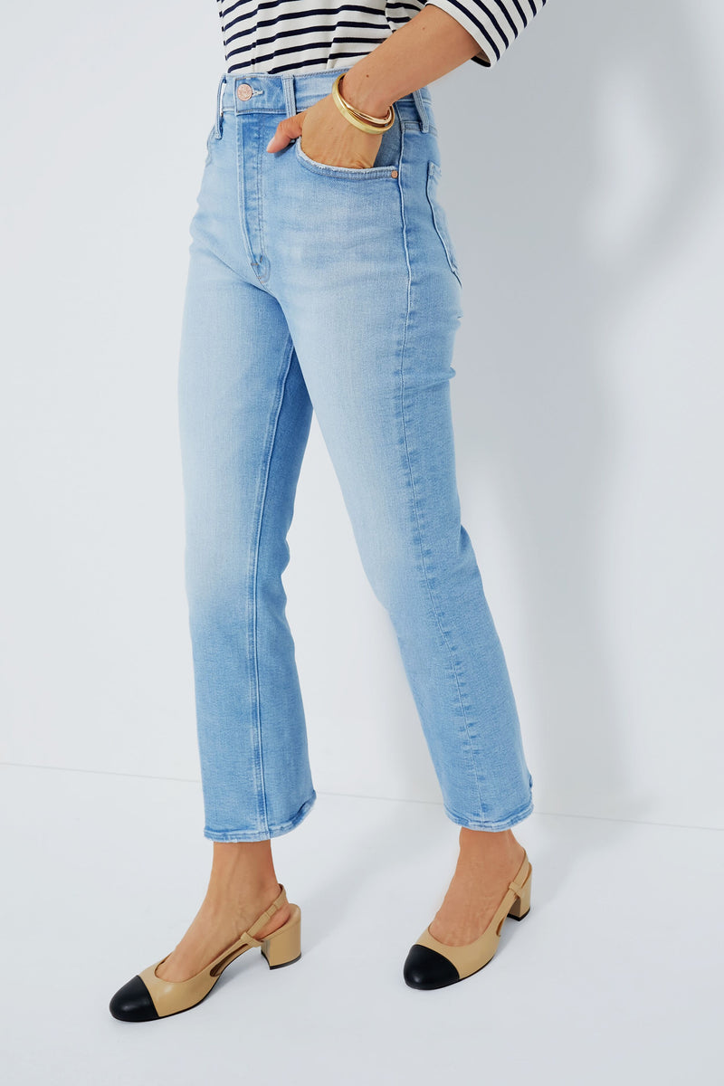 A person wears MOTHER high-rise ankle jeans in light blue, a striped long-sleeve shirt, and beige low-heeled shoes with black toe caps.