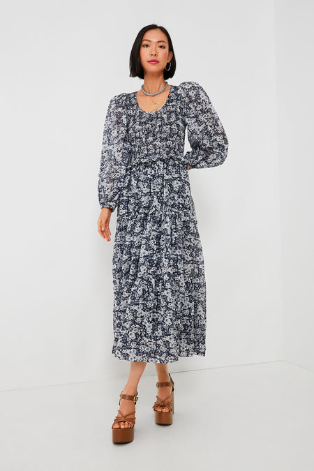 A woman models a Sea New York navy blue and white floral midi dress with a smocked bodice, paired with brown platform sandals for an elegant look.