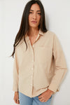 A woman with long dark hair stands confidently wearing an Alex Mill classic essential beige shirt with a chest pocket and light blue jeans.