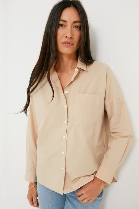 A woman with long dark hair stands confidently wearing an Alex Mill classic essential beige shirt with a chest pocket and light blue jeans.
