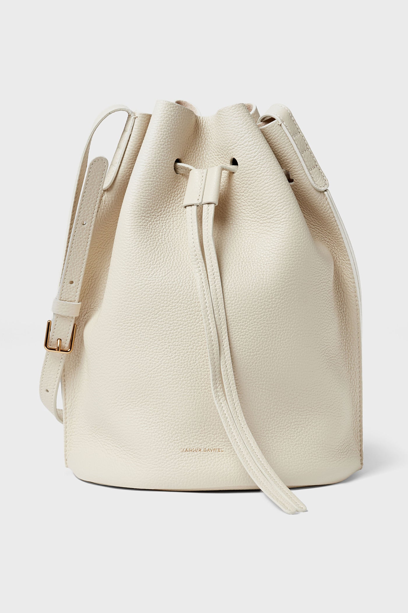 A cream-colored Mansur Gavriel bucket bag made from Italian leather features a drawstring closure and an adjustable shoulder strap.