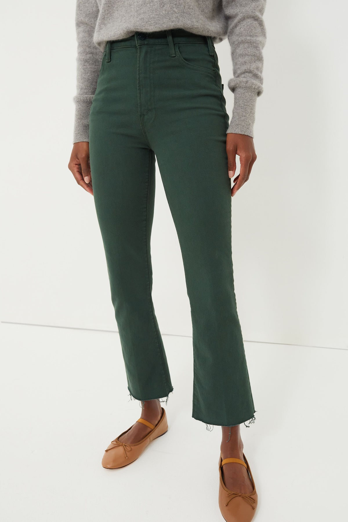 Person wearing a gray sweater, high rise ankle length green kick flare jeans with frayed hems from MOTHER, and tan ballet flats.