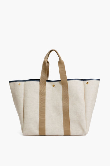 The Rue de Verneuil large beige canvas linen tote features two long tan handles, black trim at the top, and gold-tone snap details on the front—ideal for use as a work bag.