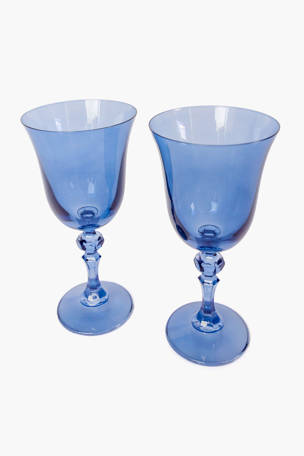 Two hand-blown goblets by Estelle Colored Glass feature wide bowls, faceted stems, and rich cobalt hues—luxurious stemware ideal for elegant occasions.
