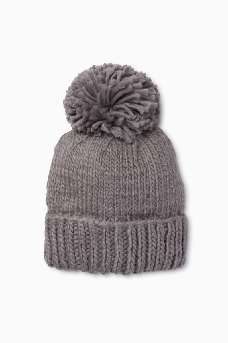 The Look by M gray pom beanie features a wide folded brim and a large pom-pom on top. This hand knit beanie adds cozy style to any outfit.