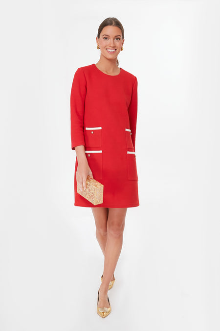 A woman wears a Tuckernuck red Francoise Mod Mini Dress with white-trimmed pockets, gold heels, and holds a textured gold clutch.