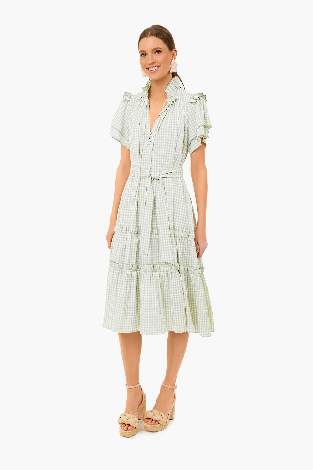 A woman stands and smiles wearing the Hunter Bell Pale Green Check Matthews Dress—a light green and white v-neck midi dress with short ruffled sleeves, a belted waist—and platform sandals.