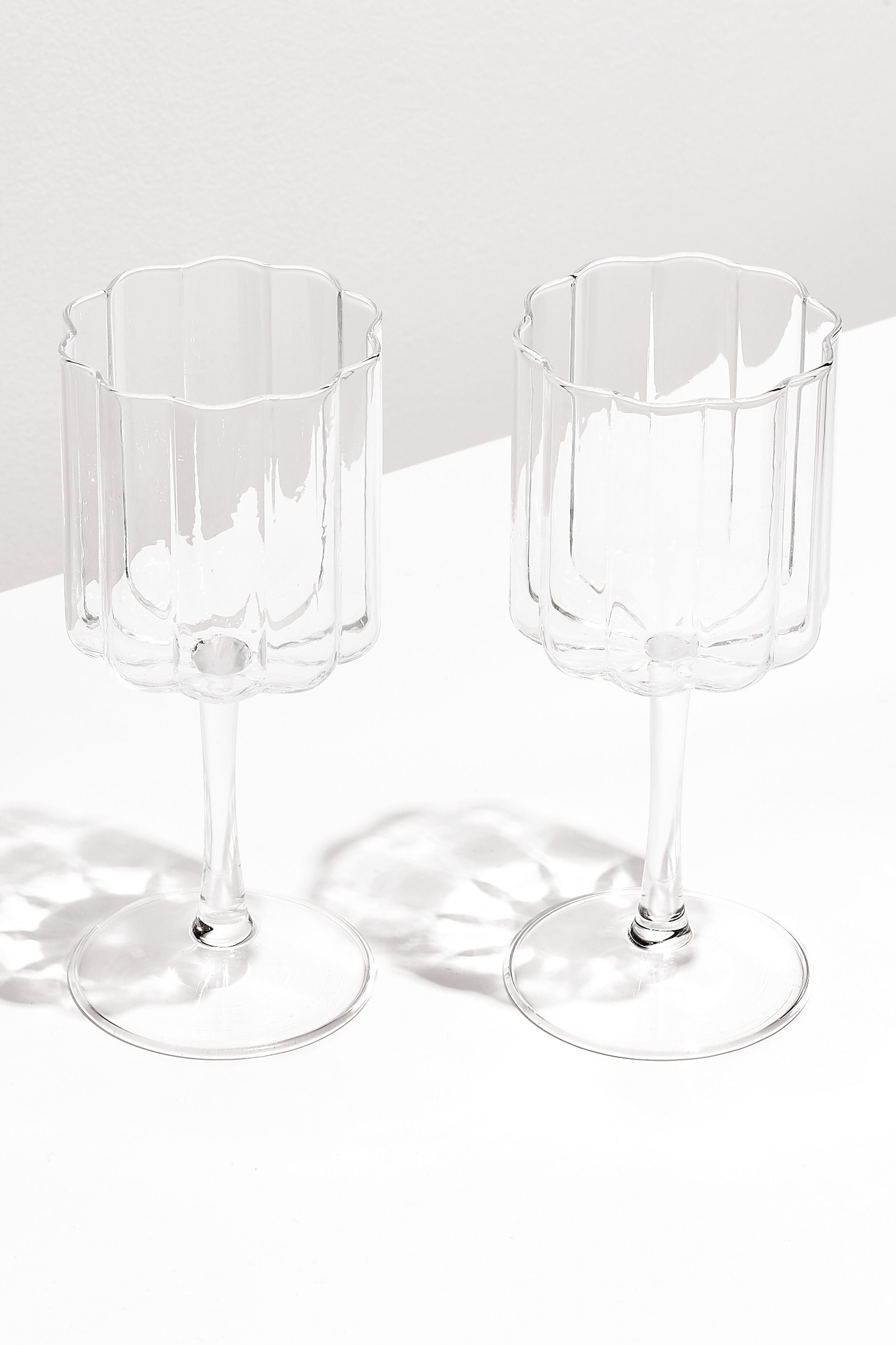 Two clear, scalloped-edge wave wine glasses by FAZEEK sit side by side on a white surface, crafted from hand-blown borosilicate glass for a sculptural homeware touch.