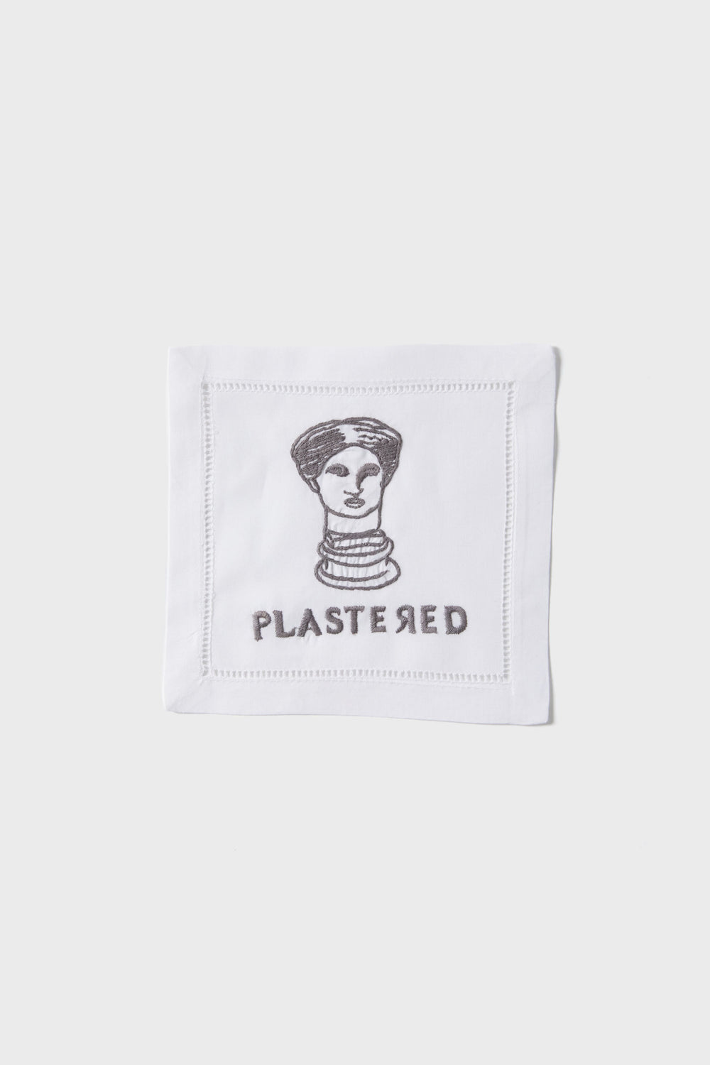 The August Morgan white linen cocktail napkin features a cheeky black line drawing of a woman’s head above “PLASTERED”—a fun hostess gift or playful addition to your next gathering.