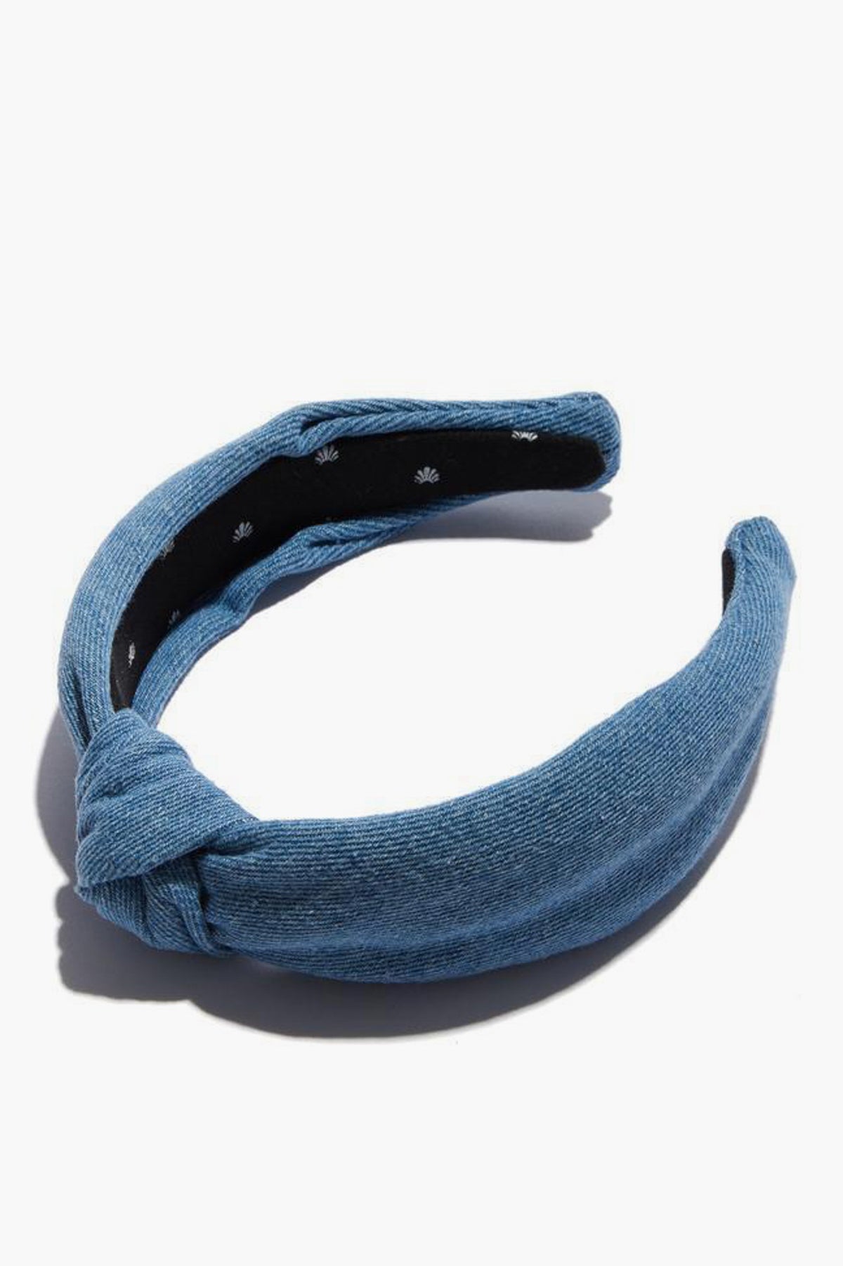 A blue textured light denim headband by Lele Sadoughi features a knotted top detail and black inner lining.