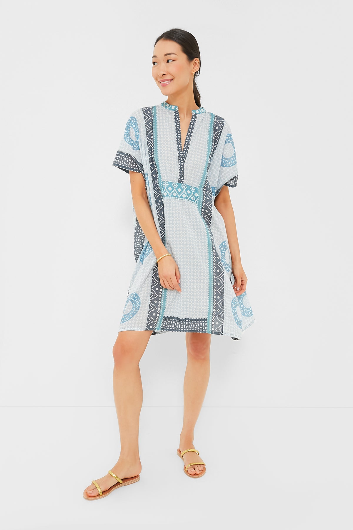 A woman wears a short-sleeved, knee-length blue and white organic cotton dress by Love Tomas by Emerson Fry, paired with yellow sandals.