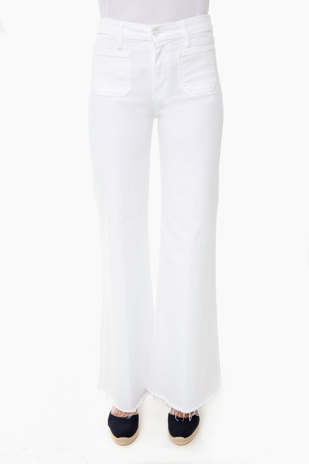 A person wears MOTHER high-rise, white wide-leg jeans with front pockets and frayed hems, paired with dark espadrille shoes.