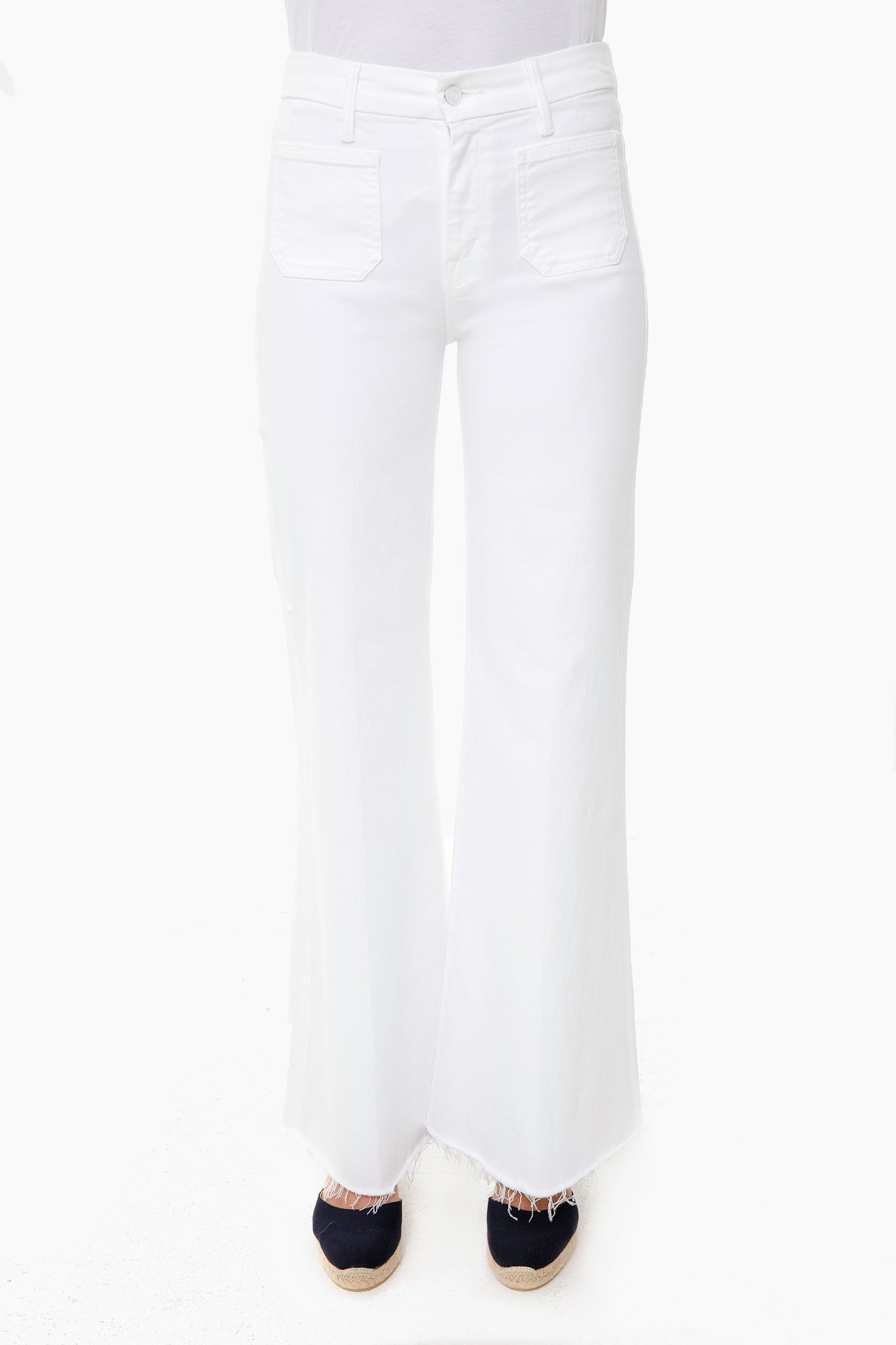 A person wears MOTHER high-rise, white wide-leg jeans with front pockets and frayed hems, paired with dark espadrille shoes.