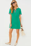 A woman in a Tuckernuck green sporty mini dress, beige loafers, and sunglasses holds a white tote bag. The dress is crafted from 100% cotton for comfort and style.