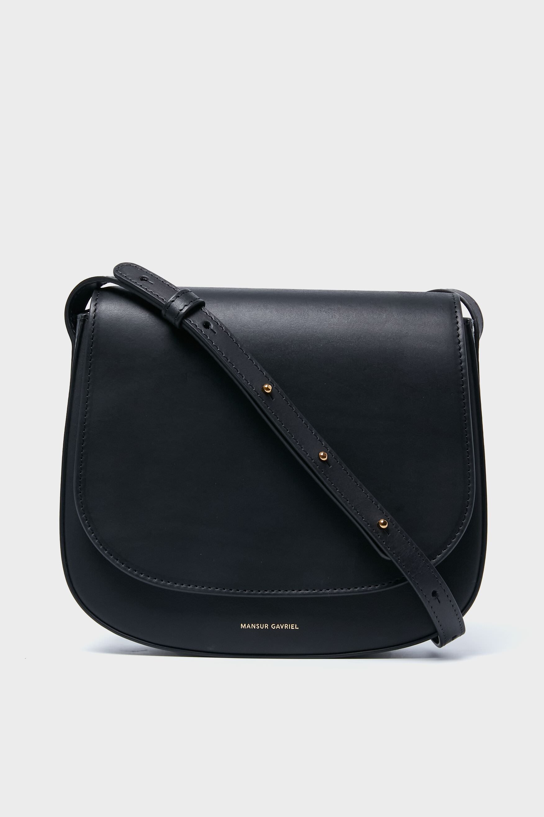 A Black Classic Crossbody bag by Mansur Gavriel, made from vegetable tanned leather with a flap closure, adjustable strap, and the brand name in gold lettering on the front.