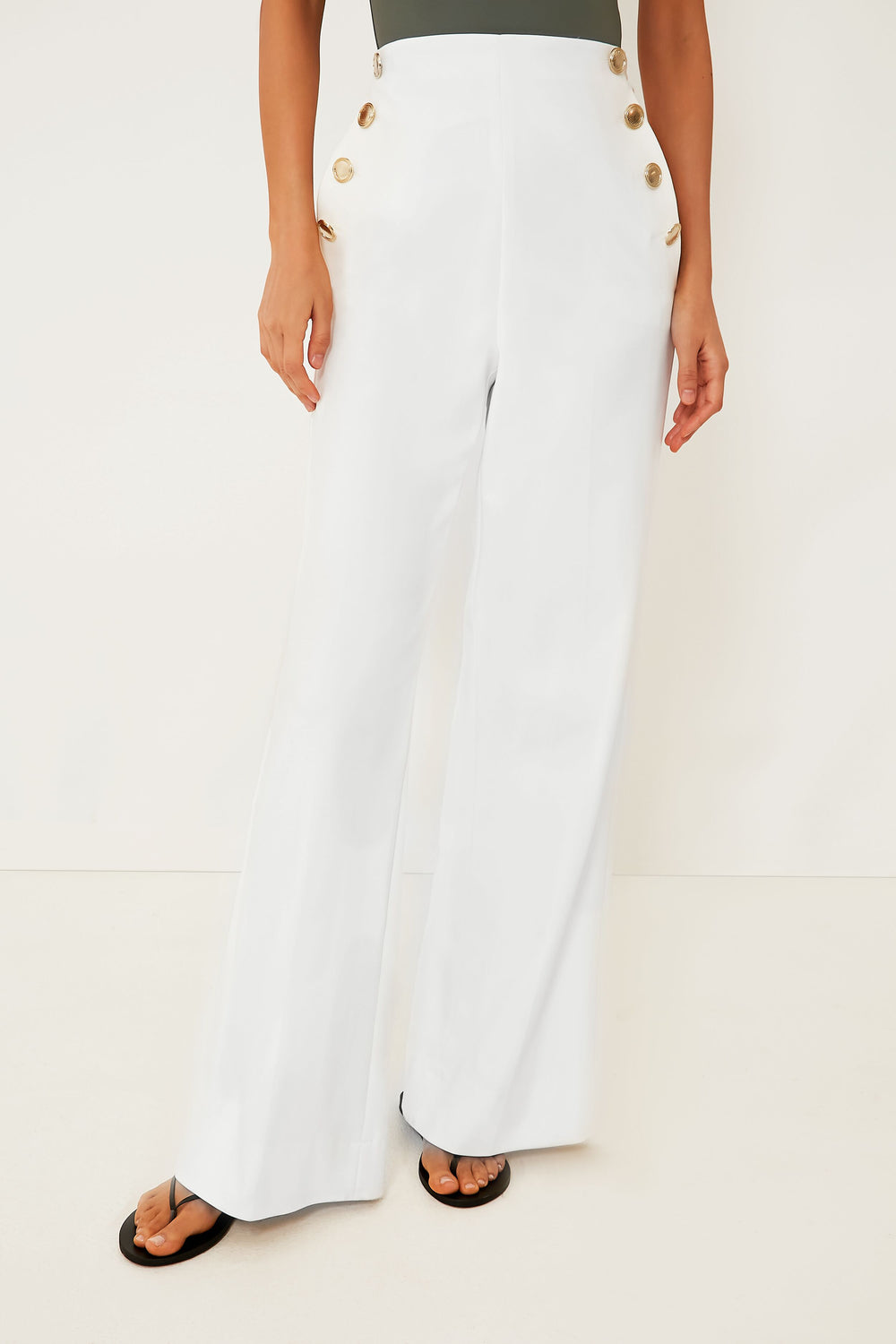 A person in Marella high waist trousers with six gold buttons, a sleeveless top, and black sandals stands confidently.