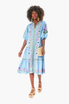 A woman in a light blue embroidered Roller Rabbit Valonia Dress with puffed sleeves, holding a straw clutch and wearing platform sandals, exudes effortless boho-chic style.
