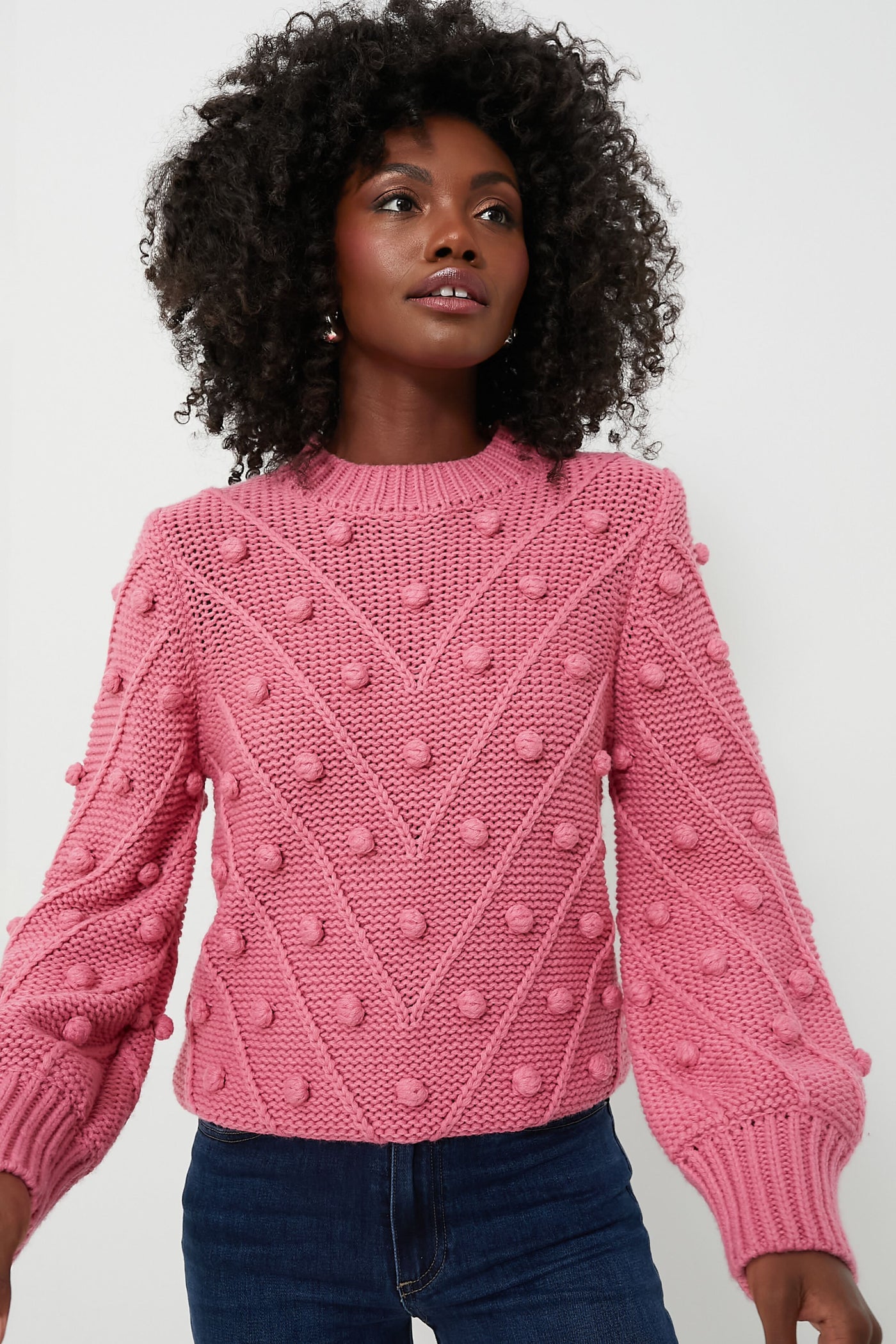 A person wears the Hyacinth House pink pompom sweater with raised bobble details and blue jeans, highlighting the cozy style of this oversized pullover.