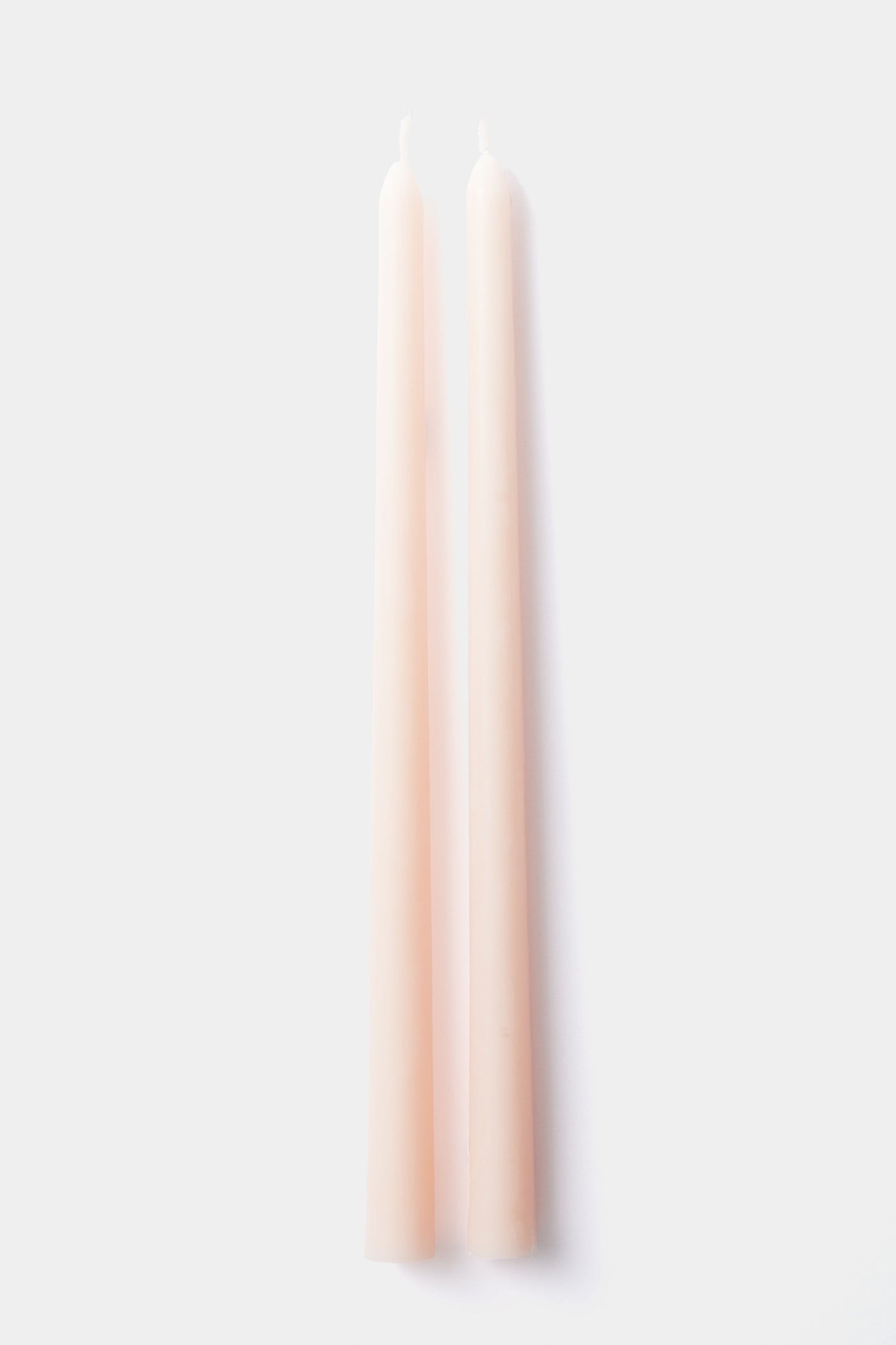 Two unlit, tall, pale pink Greentree Home taper candles stand upright side by side. These elegant hand-poured candles bring a touch of sophistication to any setting.