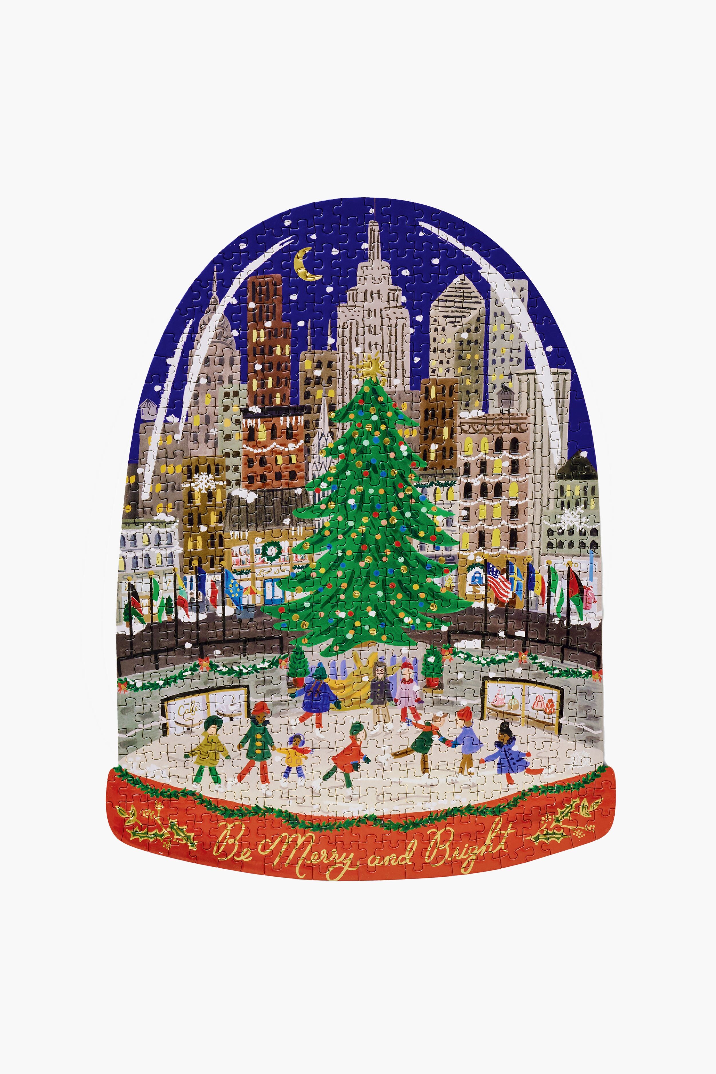 Rifle Paper Co.'s Holiday on Ice Puzzle features hand-painted cityscape art with a festive Christmas tree, ice skaters, and "Be Merry and Bright" on the base, all set inside a whimsical snow globe.