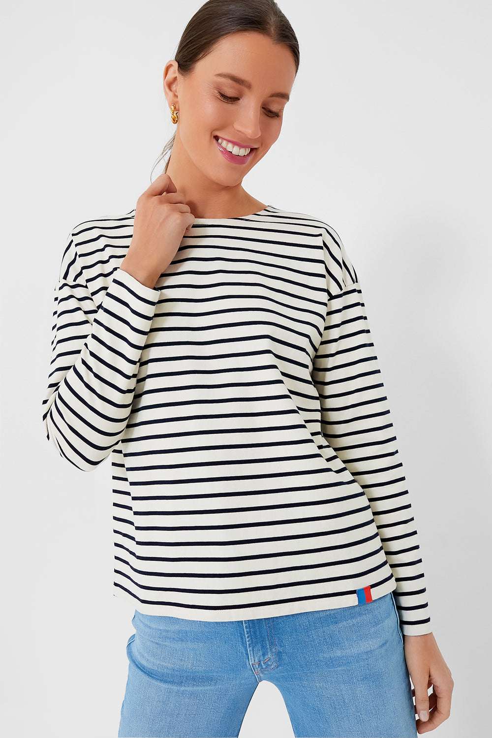 A woman smiles and looks down, wearing a KULE black and white cotton knit jersey stripe tee with light blue jeans.