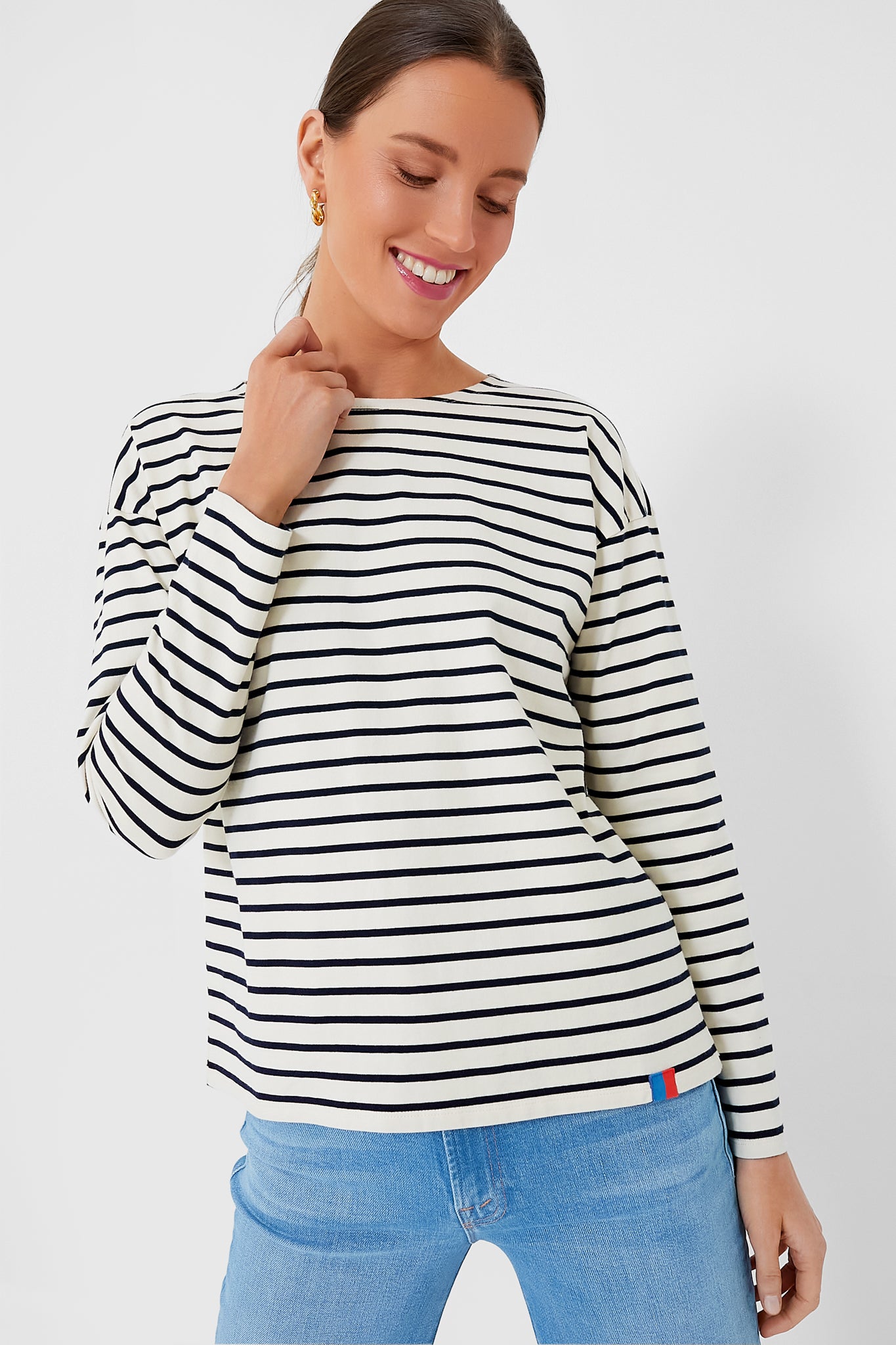 A woman smiles and looks down, wearing a KULE black and white cotton knit jersey stripe tee with light blue jeans.